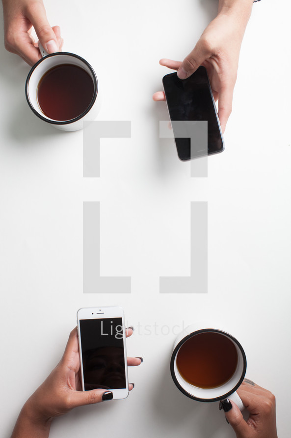 looking down at hands holding coffee mugs and cellphones 