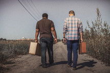 men walking down a dirt road with suitcases 