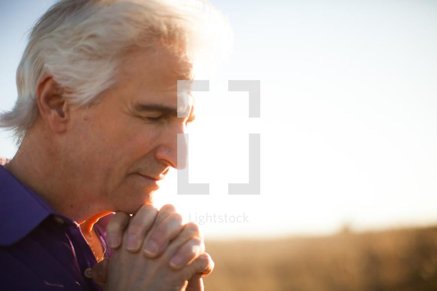 a man outdoors with praying hands 