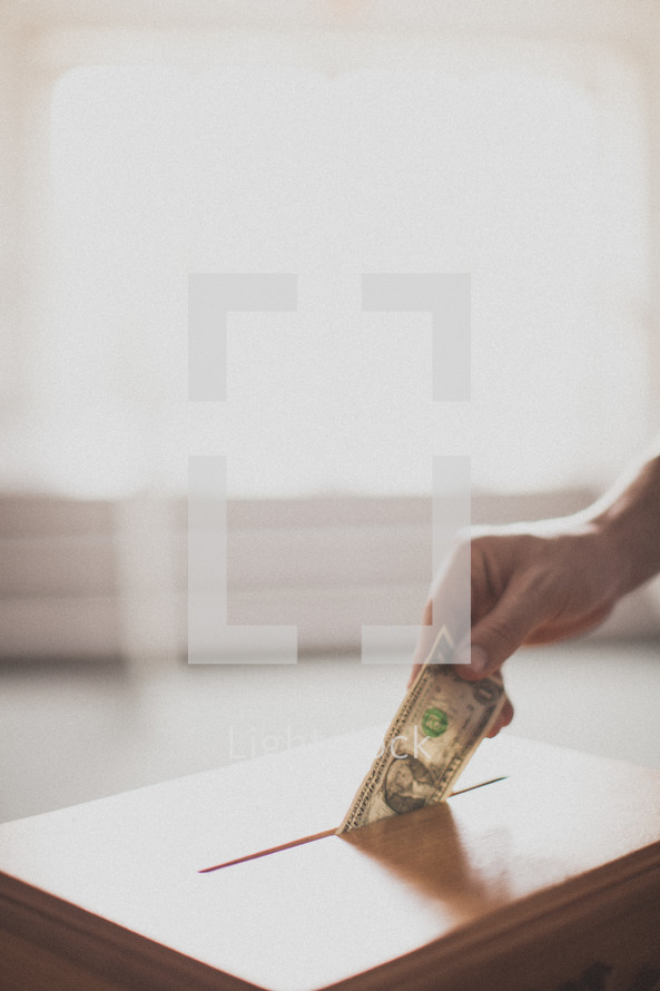 hand placing a dollar in a tithe box