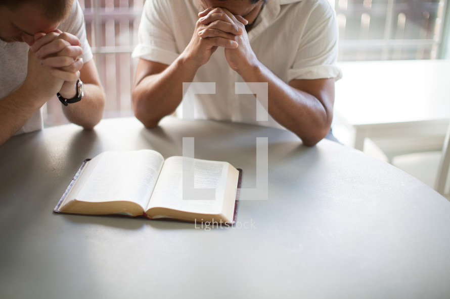 two men in prayer over a Bible 