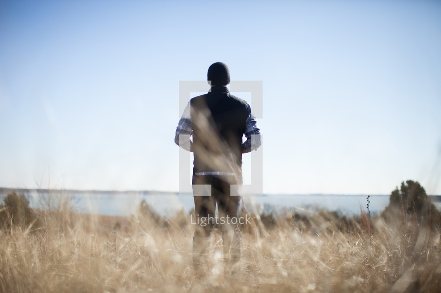 man standing in a field by a lake 