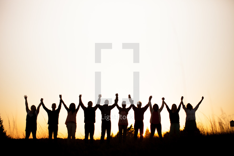 silhouette of a row of people with raised hands in praise outdoors 