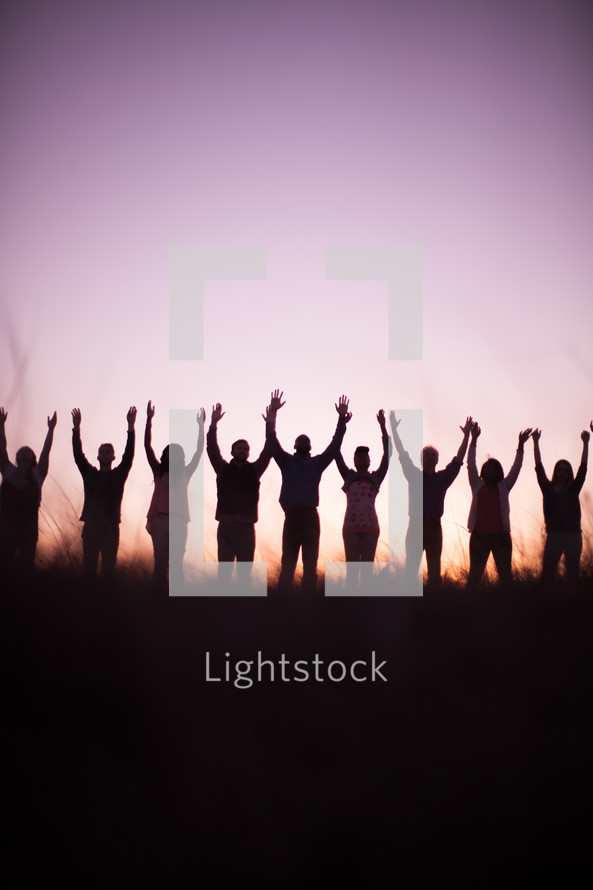 silhouette of people in a row outdoors with raised hands in praise 