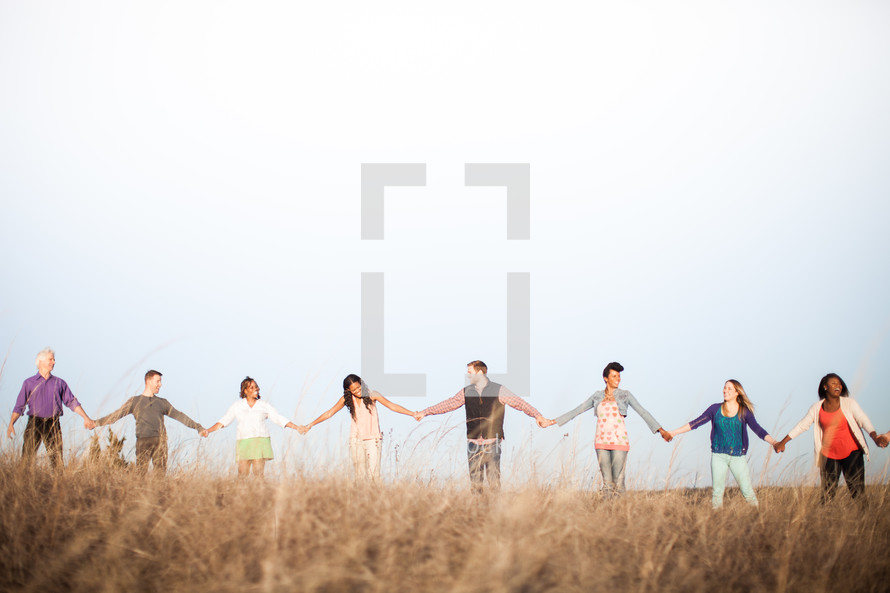group holding hands in fellowship in a field 