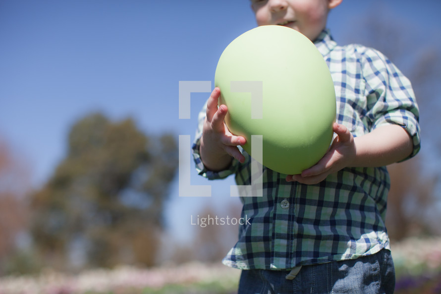 Boy holding a giant Easter egg.