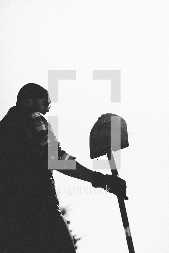 A man under a gray sky holds a shovel.