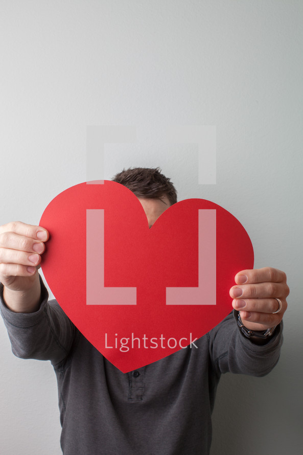 man holding a large red paper heart 