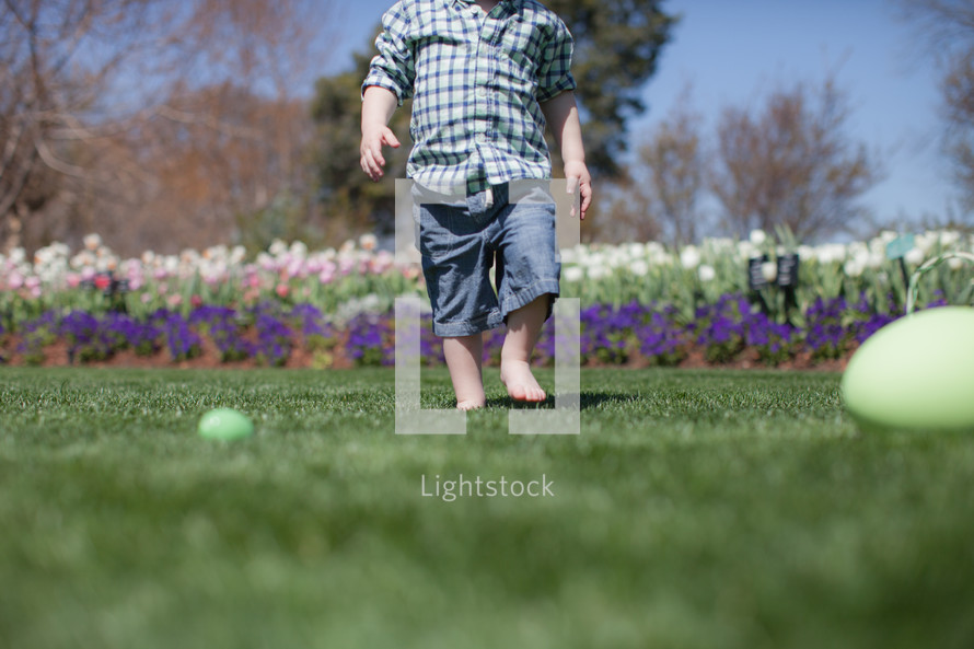 young child looking for Easter eggs in a garden of flowers