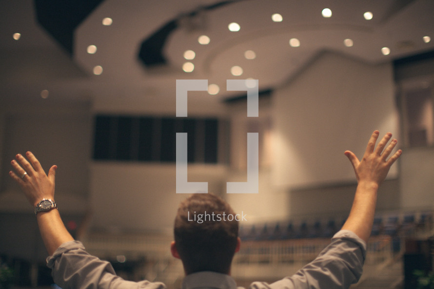 man standing in an empty church with his hands raised in worship to God 