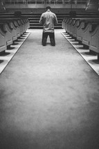 Man kneeling with head bowed in center aisle.