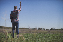 man standing in a field with raised hand