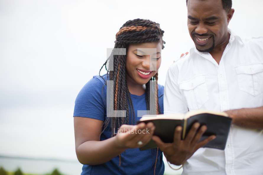 happy African-American couple reading a Bible together outdoors 