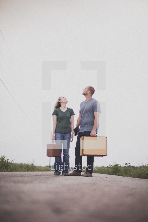 Couple with a Bible and suitacse standing in the middle of the road looking up.