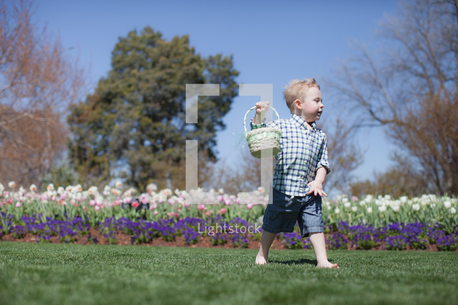 Young barefoot boy, with Easter basket, in a garden of flowers