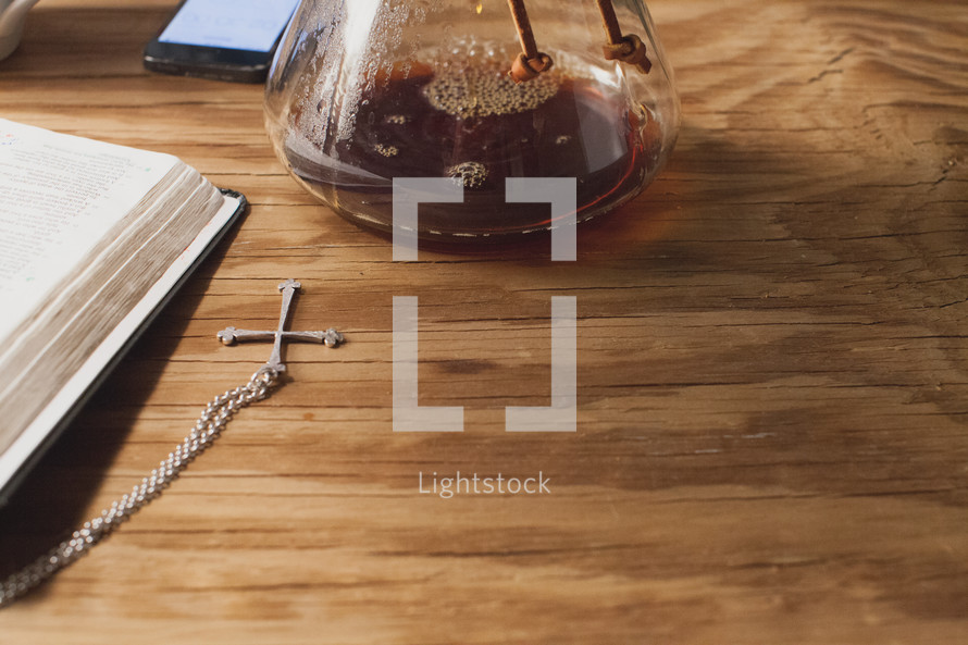 Coffee in a carafe near a Bible and cross pendant on a wood table.