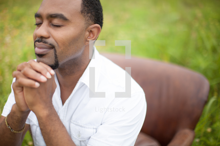 man in prayer sitting in a chair outdoors 