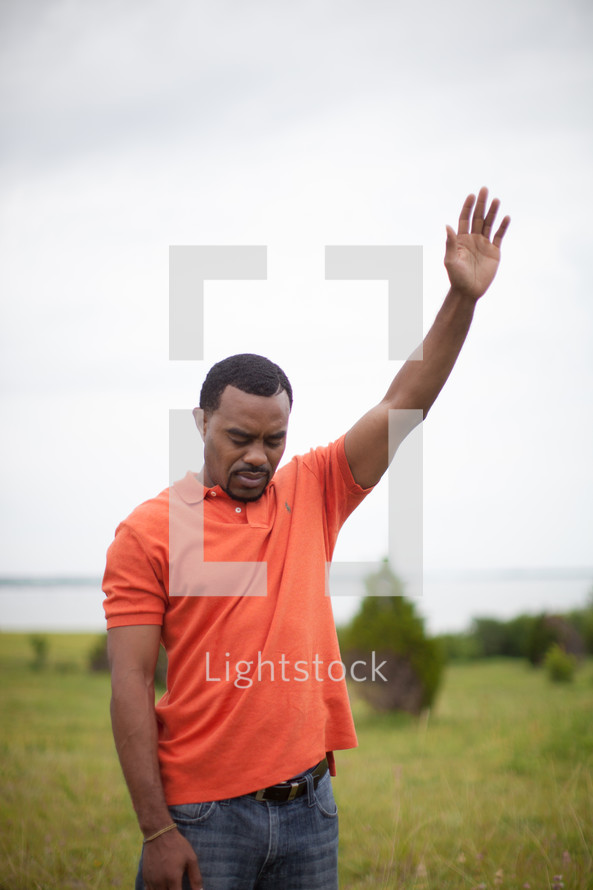 man standing in a field with his arm raised to God 