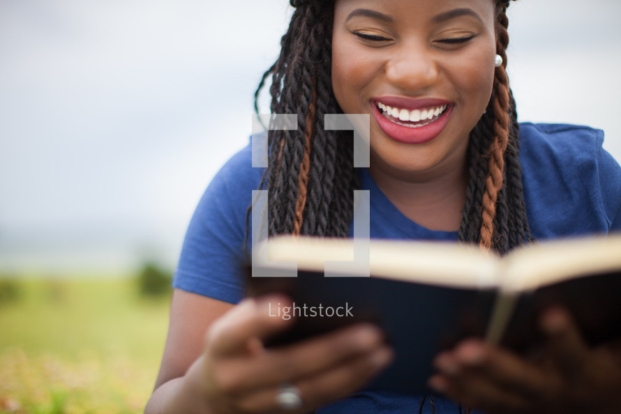 smiling woman reading a Bible outdoors 