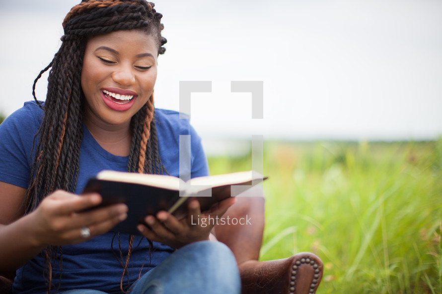 joyful African-Ameican woman reading a Bible outdoors 