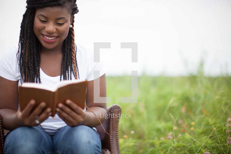 woman reading a Bible outdoors in a chair in a field 