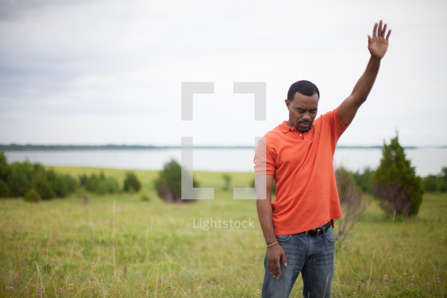 man standing in a field with his hand raised to God 