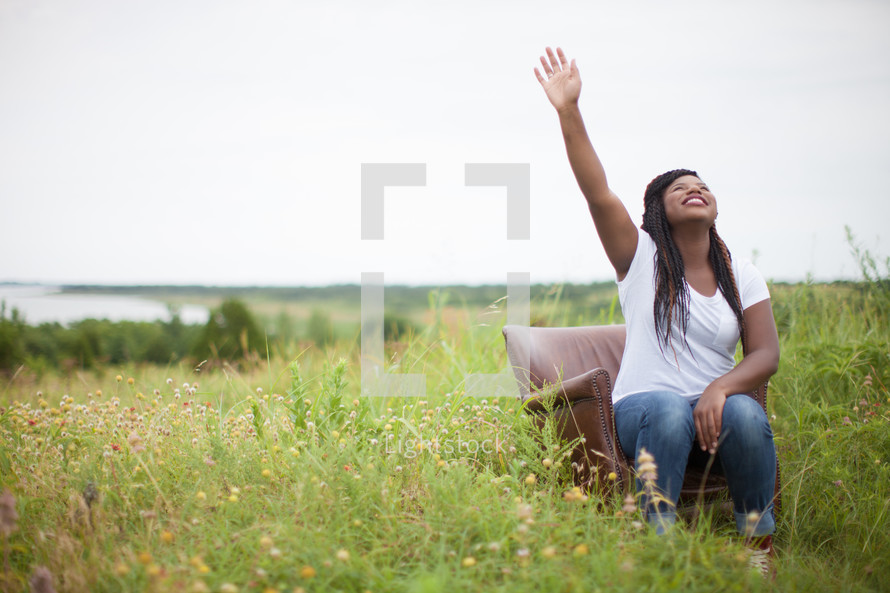 woman sitting in a chair outdoors with her arm raised to God 