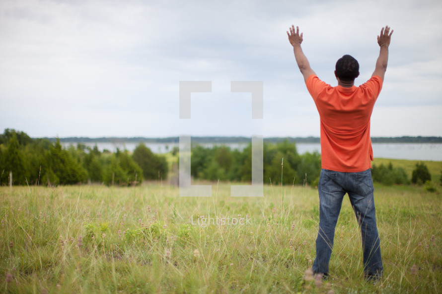 man standing in a field with hands raised to God 