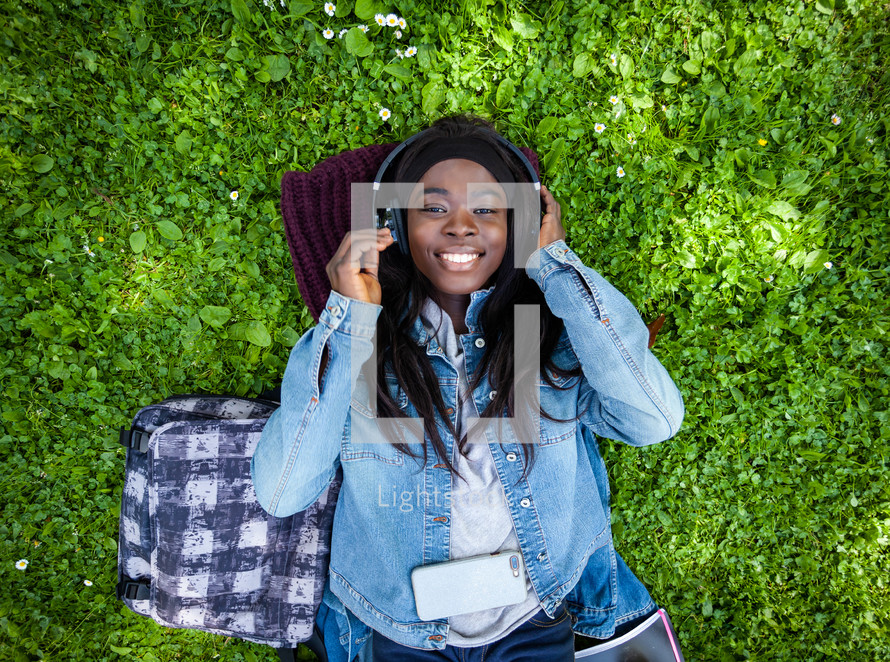 woman lying on green grass listening to music with headphones.