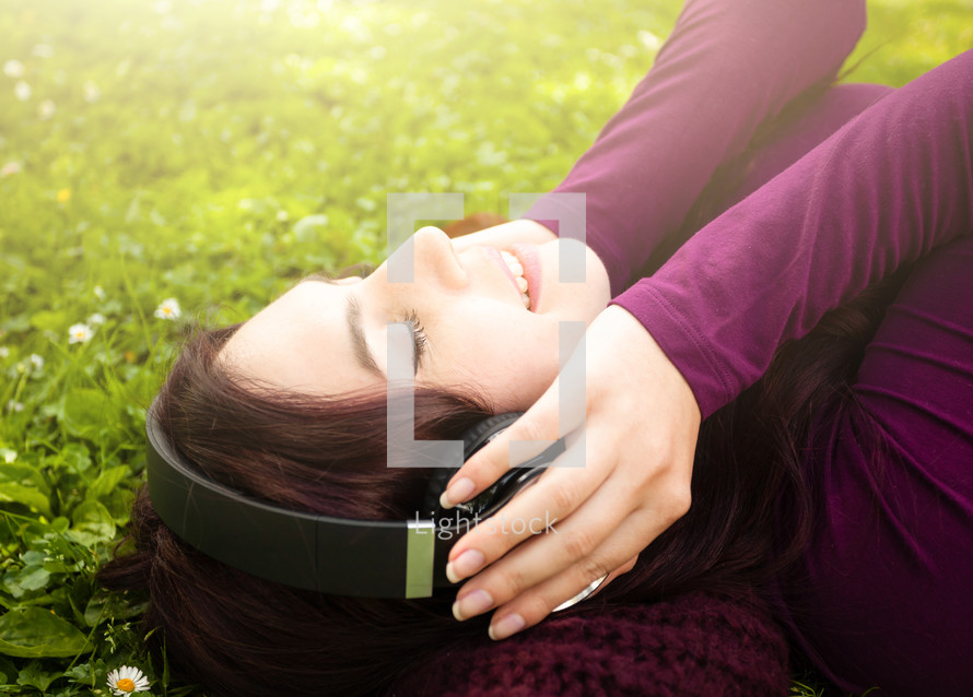 young woman listening to headphone in the grass