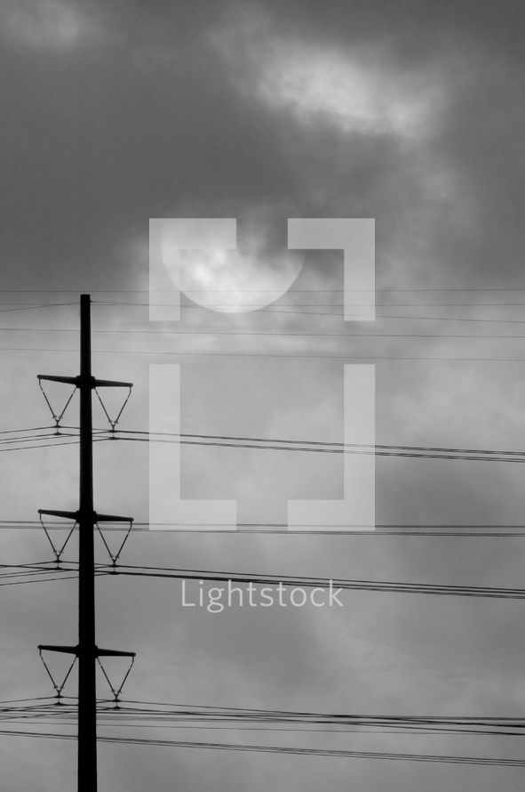power lines, sun and clouds in the sky in black and white