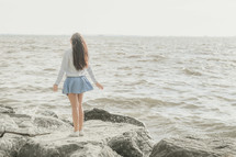 girl standing on a rocky shore looking up to God 