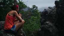 a woman taking in the view sitting on a rock on a mountaintop 