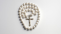The Rosary with a string of pearl beads with a silver cross and the figure of Jesus Christ. Set against a white studio background, 