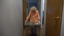 An elderly woman walking in a hallway with her walker
