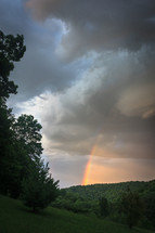 Rainbow through dark storm clouds over mountainous forest in West Virginia vertical