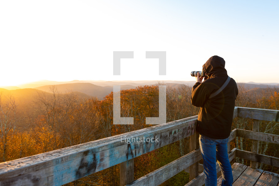 Photographer taking pictures of sunrise and autumn forest atop Bickle Knob wooden watchtower outlook in West Virginia 