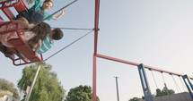 Children riding swings together at a public playground.
