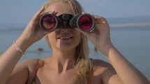 View of blond woman watching with binoculars against blurred sea