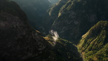 Clouds in a green valley surrounded by majestic rocky mountains in Madeira, aerial view