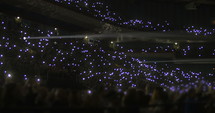 Crowd of people at concert waving small flashlights.
