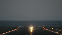 A frontal shot of a lighted runway and an airplane, that is riding to the camera and then takes off