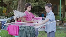 Three kids taking off laundry from the hanging line to the basket