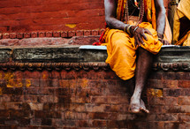 A man sitting on a brick wall wearing traditional clothing 