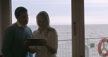 Man and a woman looking at a smart tablet with an ocean view behind them.