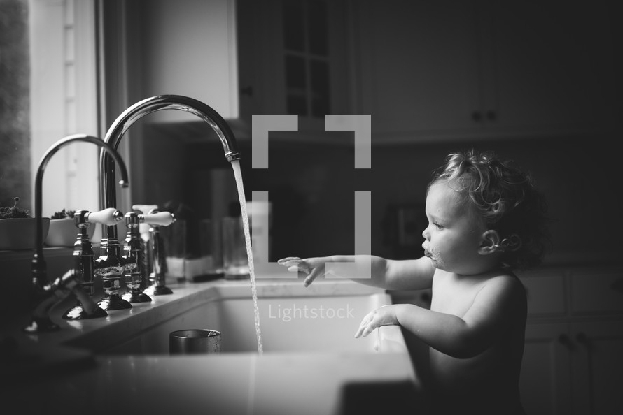 toddler playing in water at the kitchen sink 