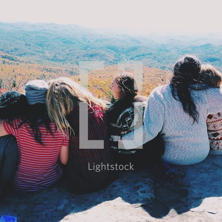 A group of girls sit closely together on a rock ledge.