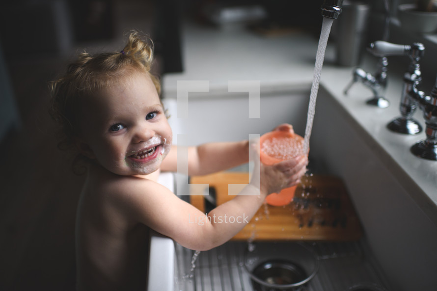 a toddler playing in water at the kitchen sink 