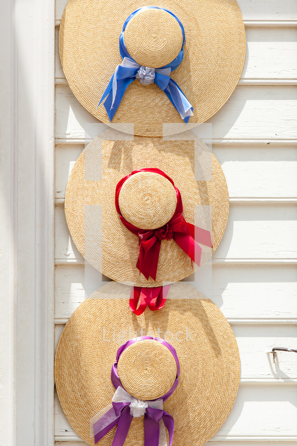 Three old fashioned woven straw hats with colorful ribbons hanging on white house in Williamsburg Virginia