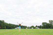 a woman standing in a field with lifted arms 